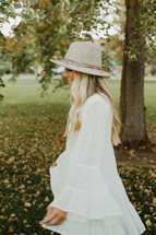 a young woman in a white dress and hat twirling outdoors 
