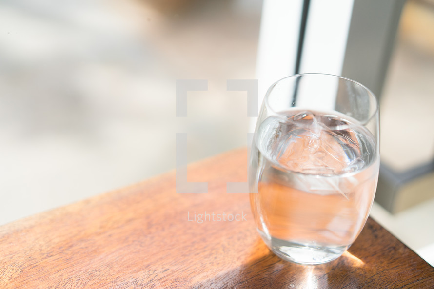 glass of water at the edge of a wood table 