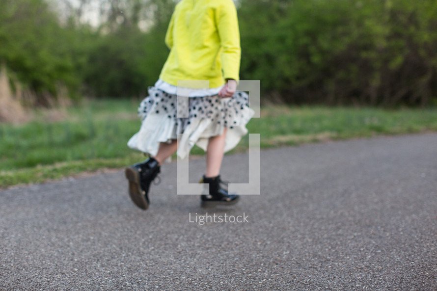 a girl child in boots and skirt stomping down a paved path 