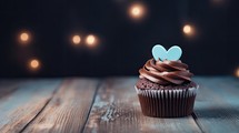 Chocolate cupcake with blue heart on top and lights on wooden background