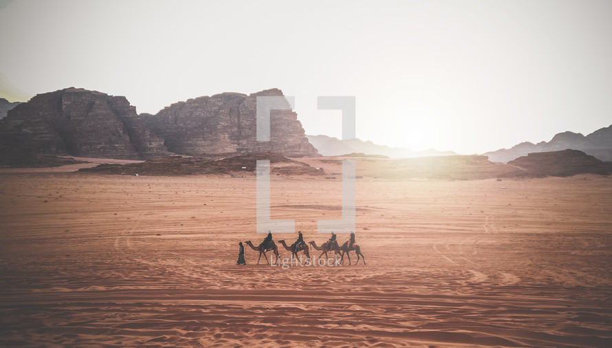 Jordan, Wadi Rum. Caravan of camels with drovers in the desert, rock mountains at sunset.