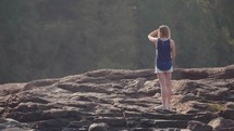a woman standing on a rocky shore looking out 