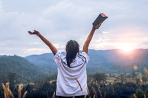 Young woman holding and lift up bible to sky outdoors with light sunset background,christian concept.