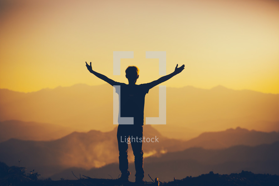 silhouette of a young man with outstretched arms at sunset 