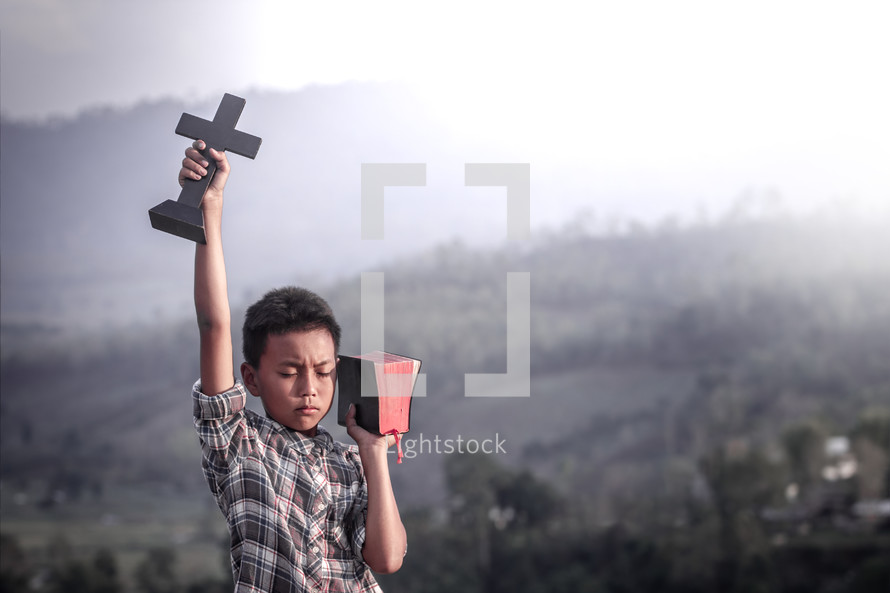 a child with a raised hand holding a Bible and cross 