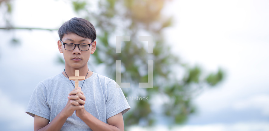 a young man praying holding a cross 