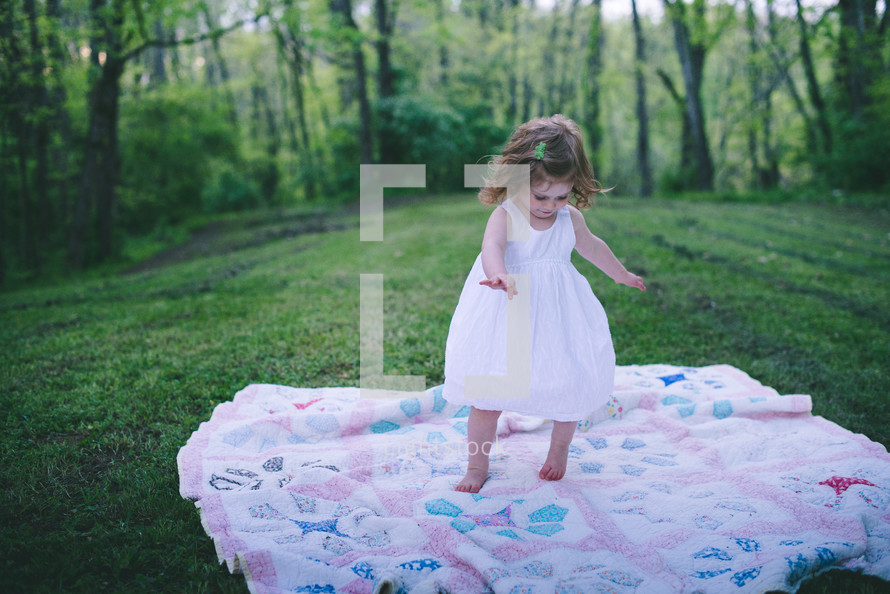 little girl dancing on a blanket in the grass