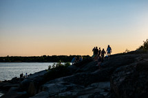 people sitting on rocks along a shore at sunset 