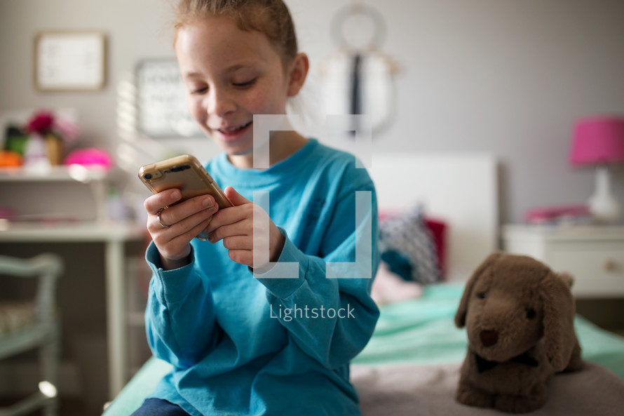 a girl sitting on a bed looking at a cellphone 