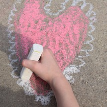 a child drawing a Valentine's heart on concrete with sidewalk chalk 