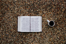 open Bible and coffee mug on gravel