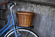 Bicycle with a basket parked against a cement wall.