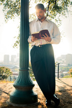 a man reading a Bible leaning on a pole