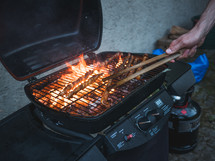 a man's hand with tongs, turning some meat on a bbq