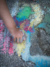 a child's hand draws on the pavement with colored chalk