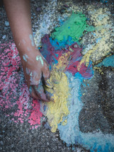 a child's hand holding a piece of colored chalk drawing on the pavement