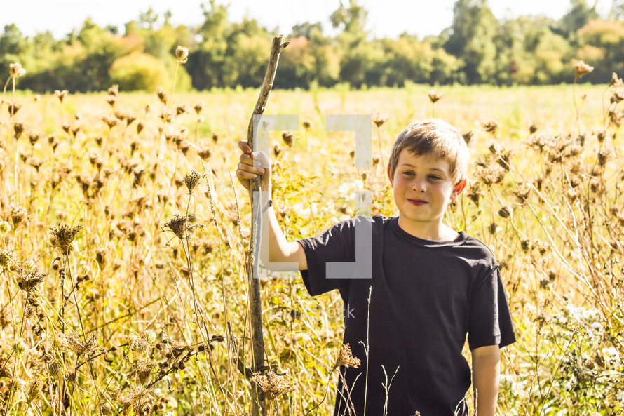 a boy with a walking stick standing in a field 