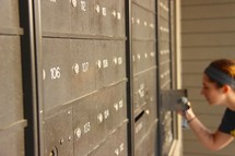 a woman checking for mail at an apartment mail room 