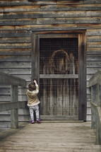 Little girl trying to reach up to open an old wooden door.