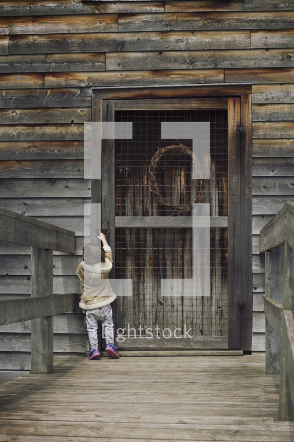 Little girl trying to reach up to open an old wooden door.