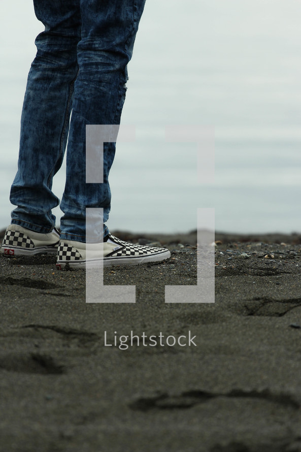 feet in sneakers standing on black sand 