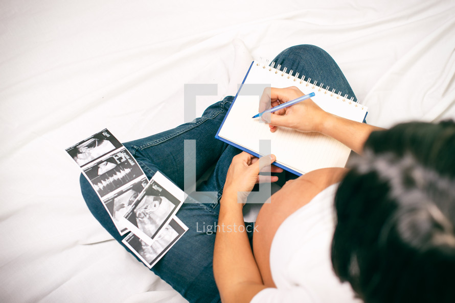 Pregnancy dairy. Pregnant woman writing thoughts down in notebook for memory, sitting in bed with baby sonography