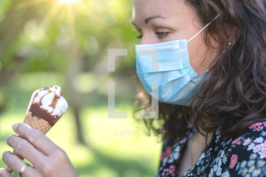 Beautiful girl wearing a face mask looking down at an ice cream in her hand