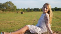 Life in the countryside. Portrait of a smiling blonde girl lying on a haystack. Happy childhood. Adorable little girl in a august field with haystacks. Summer holidays, ecology and health.