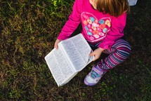 a toddler holding an opened Bible in the grass