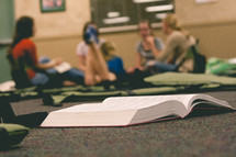 Open book laying on the floor with a group of people sitting on the floor in the distance