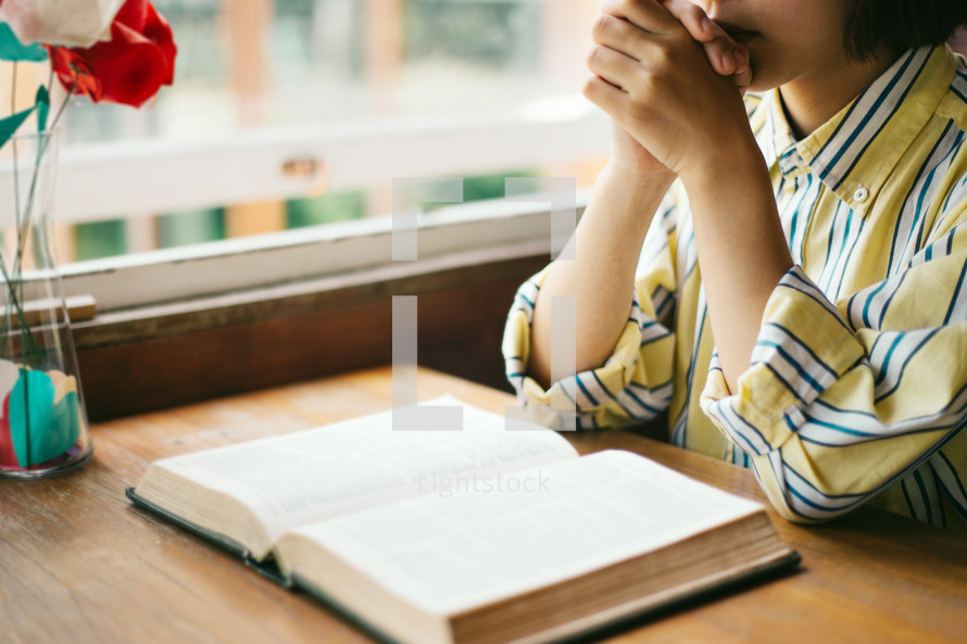 a woman sitting at a table praying over an open Bible 