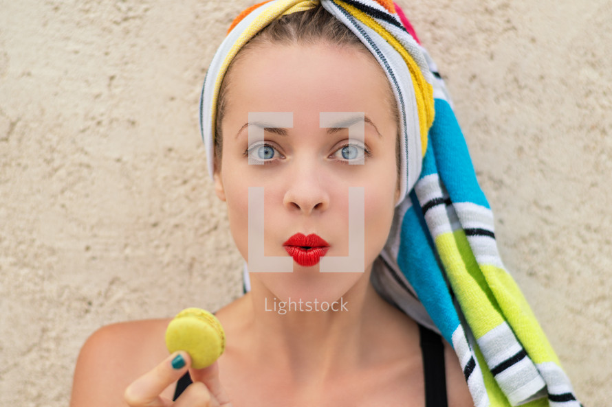 woman with her hair wrapped in a towel holding a macaron 