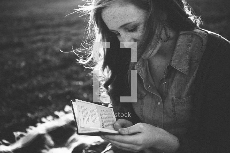 teen girl sitting on a blanket reading a pocket Bible