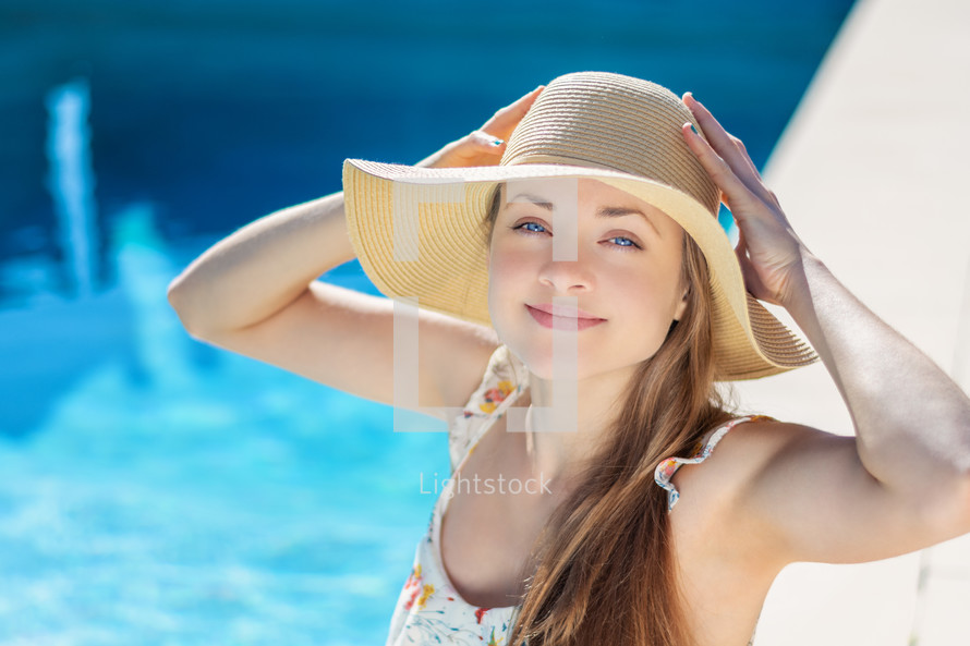 young woman in sunhat sitting by a pool 