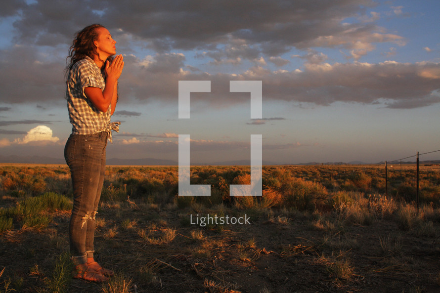 a girl praying outdoors at sunset 