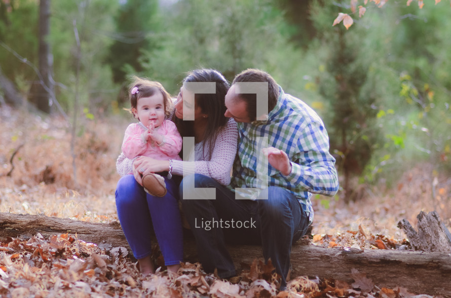mother, father, and toddler sitting on a fallen tree in fall 