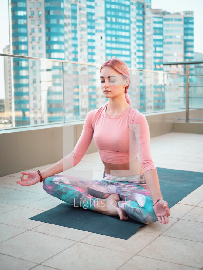  Young slim woman with pink dyed hair doing yoga practice on terrace of modern city. Girl keeping fit and healthy body relaxing on rooftop during practice pose