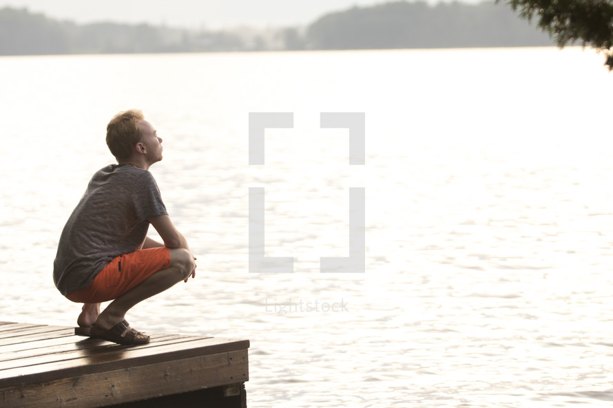 Teenager sitting on dock and praying with head looking up