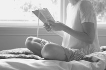 teen girl sitting on a bed reading a Bible 
