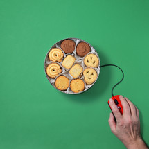Bin of cookies with computer mouse and hand on a green background