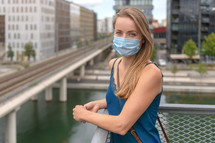 Urban city lifestyle. Young beautiful woman with face mask in modern residential district.