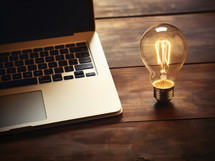 Laptop and light bulb on wooden table. Business idea concept.