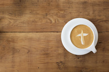 Cross shape in a latte drink on a wooden table.