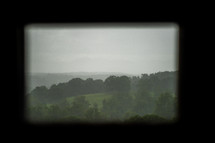 view of a foggy hillside through a window 