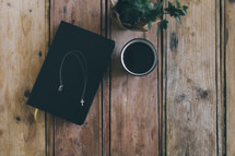 cross necklace on a Bible, coffee cup, and house plant 