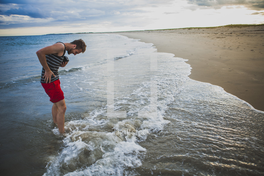 man getting his feet wet in the ocean on a beach 
