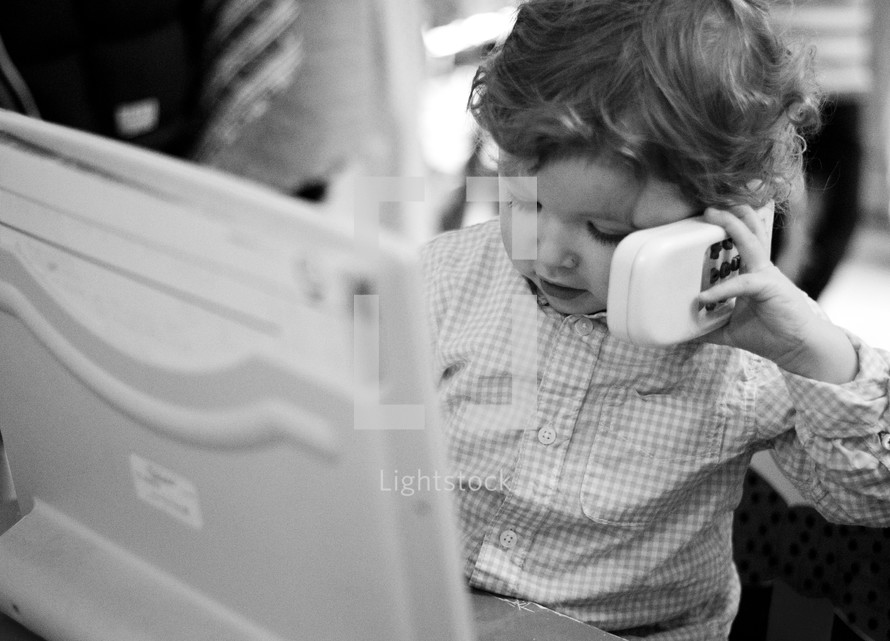 toddler boy on the phone in front of a laptop computer 