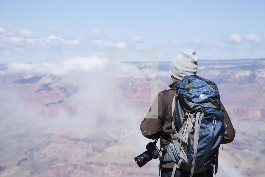 a man with a backpack and camera looking down at the canyon below 