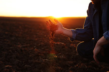 Male farmer's hand holds a handful of dry ground and checks soil fertility and quality before sowing crops on plowed field at sunset. Cultivated land. Concept of organic agriculture and agribusiness.