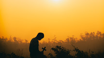 silhouette of a man praying at sunset holding a cross 
